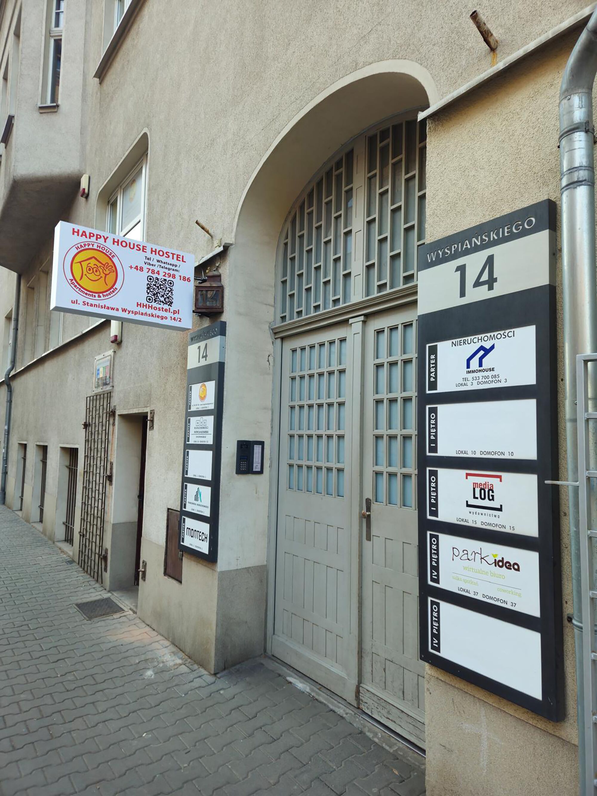 A building with a sign for Happy House Hostel, a gated entrance, and multiple business signs on the wall.