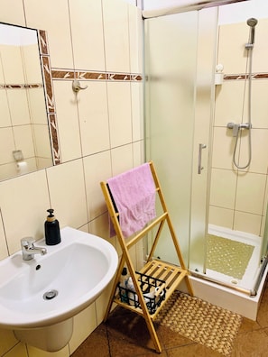 A bathroom with a sink, a mirror, a shower with a glass door, and a wooden rack holding a towel. - Happy House Hostel. Poznan (Poznan)
