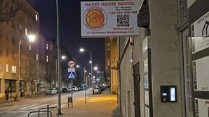 Un hostal amb una placa publicitària de Happy House Hostel, dades de contacte i un codi QR.
