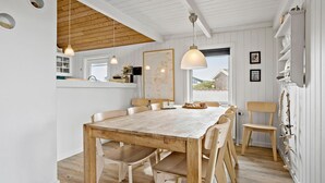 A dining area with a wooden table and chairs, a hanging light fixture, and a view of the outside through a window. - Awesome home in Thisted with sauna (Thisted)