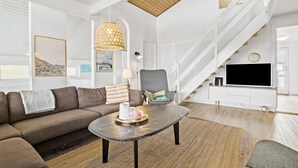 A modern living room with a sofa, a coffee table, a chair, and a TV. There is a staircase leading to another level. - Awesome home in Thisted with sauna (Thisted)