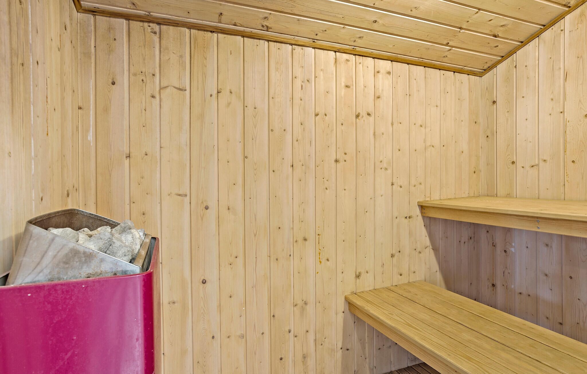 Ett ångrum med träväggar, en bänk och en rosa behållare.