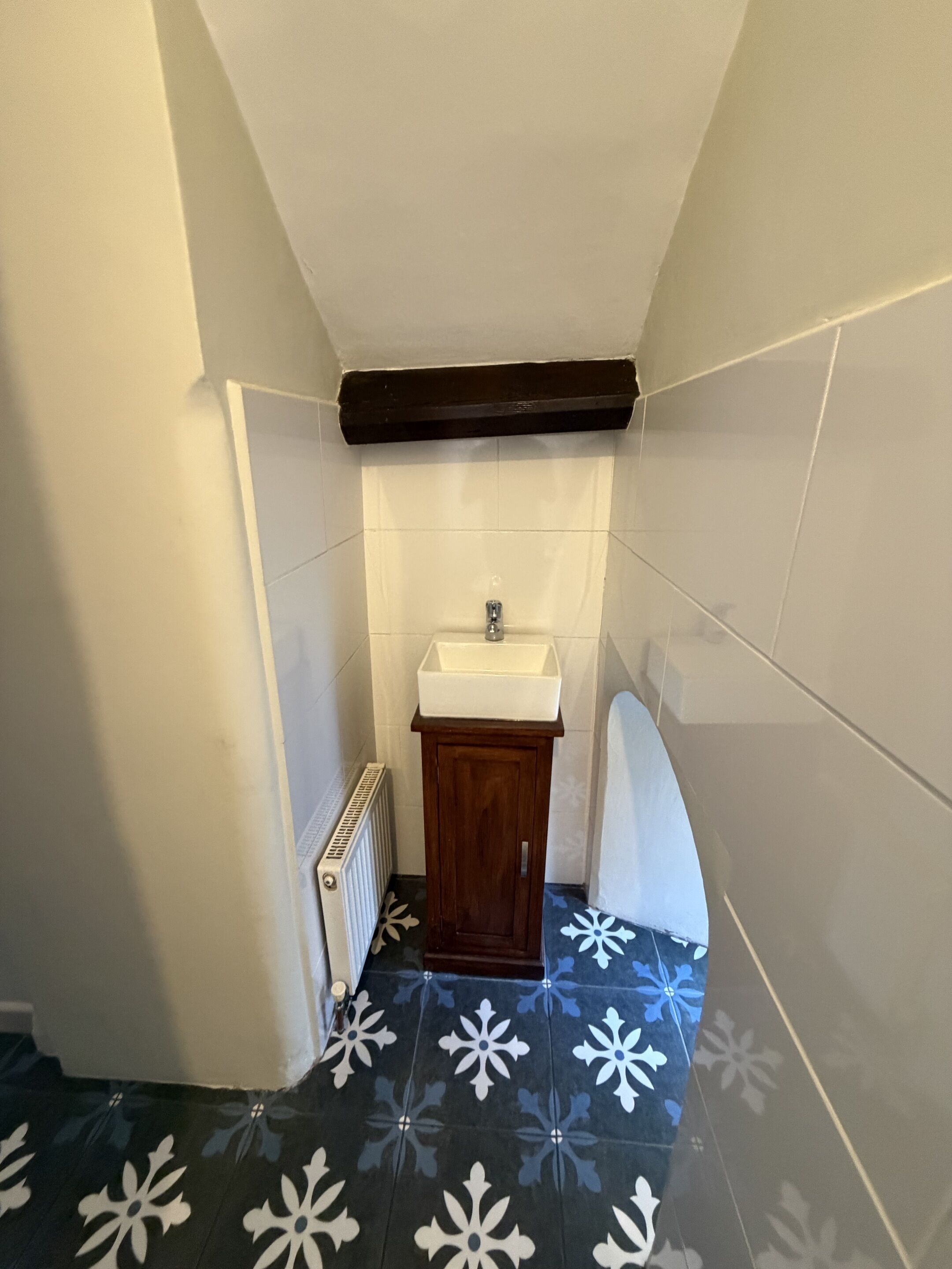 A small bathroom with a white sink, wooden cabinet, and a radiator.