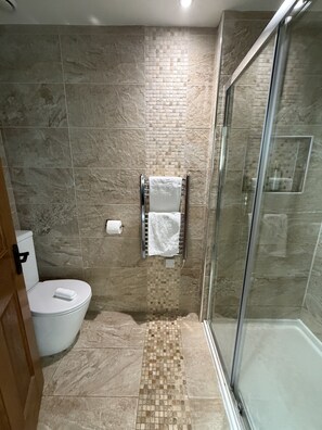 A bathroom with a toilet, a shower with a glass door, and a tiled floor. - St Nicholas  (Shrewsbury)