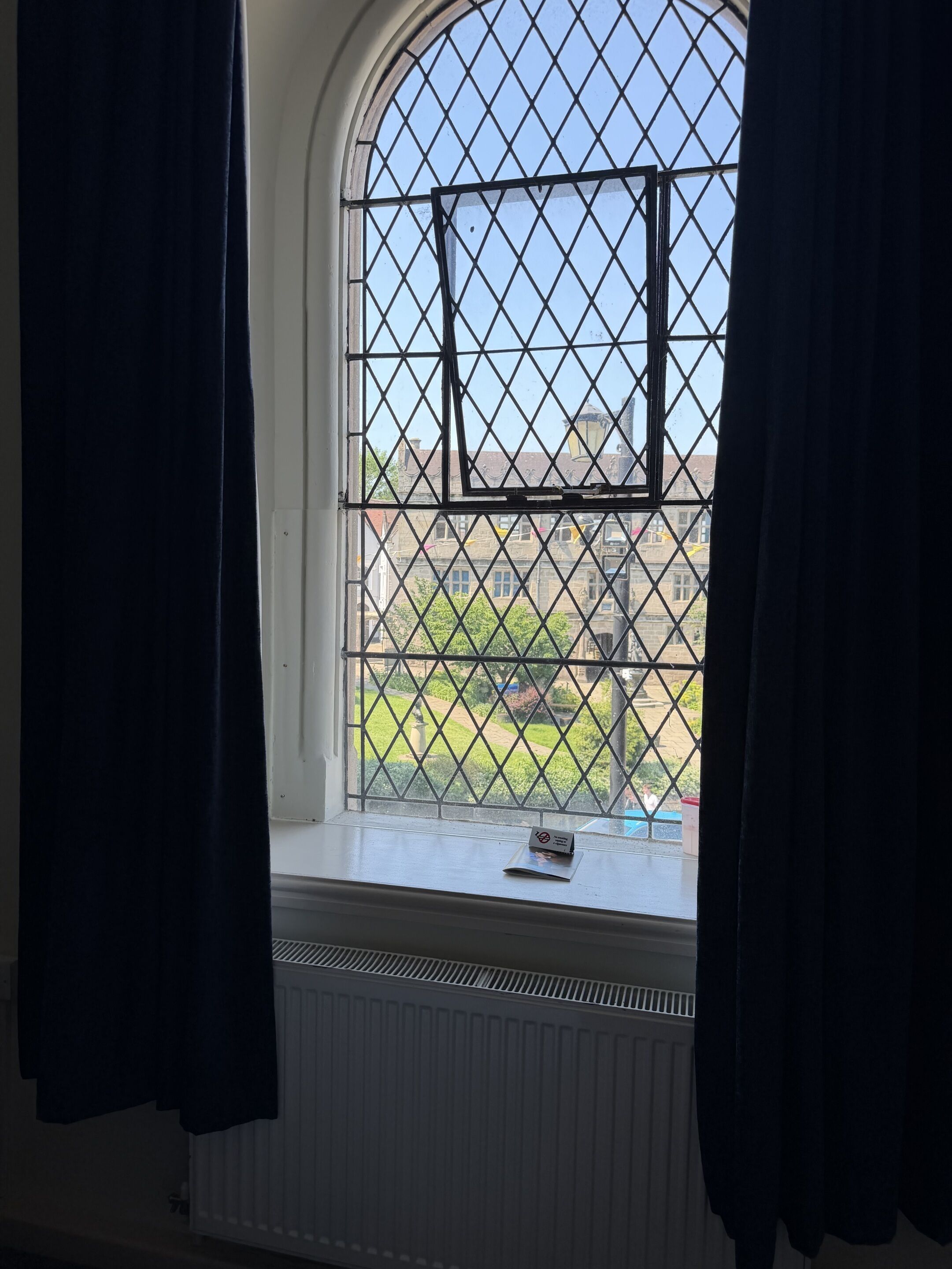 A room with a large arched window, a radiator below, and a small card on the windowsill.