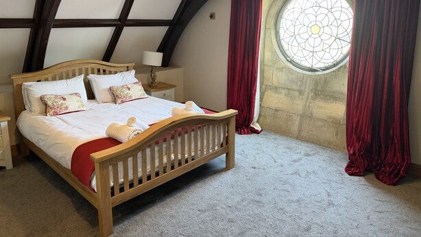 Een slaapkamer met een houten bed, nachtkastje, lamp, raam met gordijnen en een stenen muur.