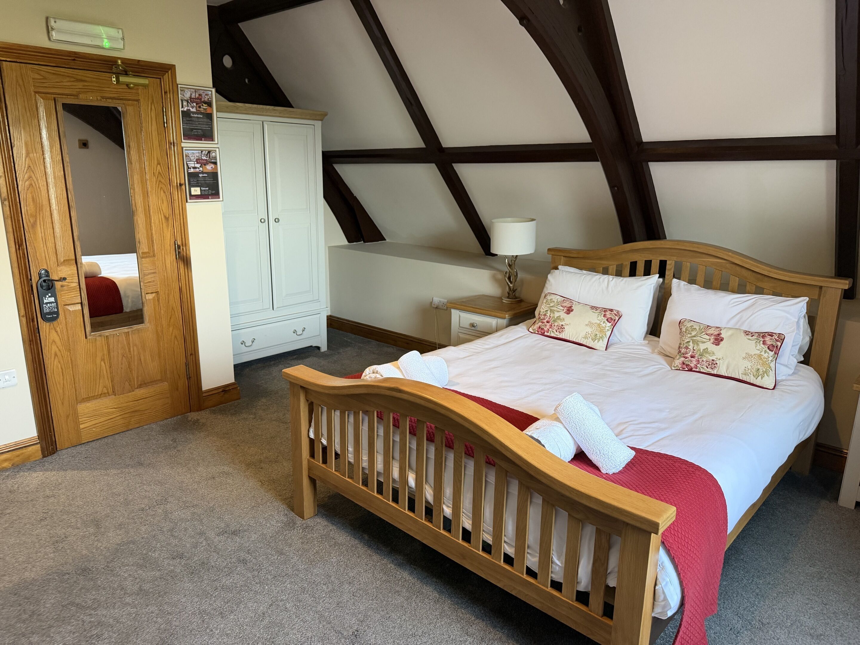 Une chambre avec un lit en bois, une armoire, un miroir et un plafond avec des poutres apparentes.