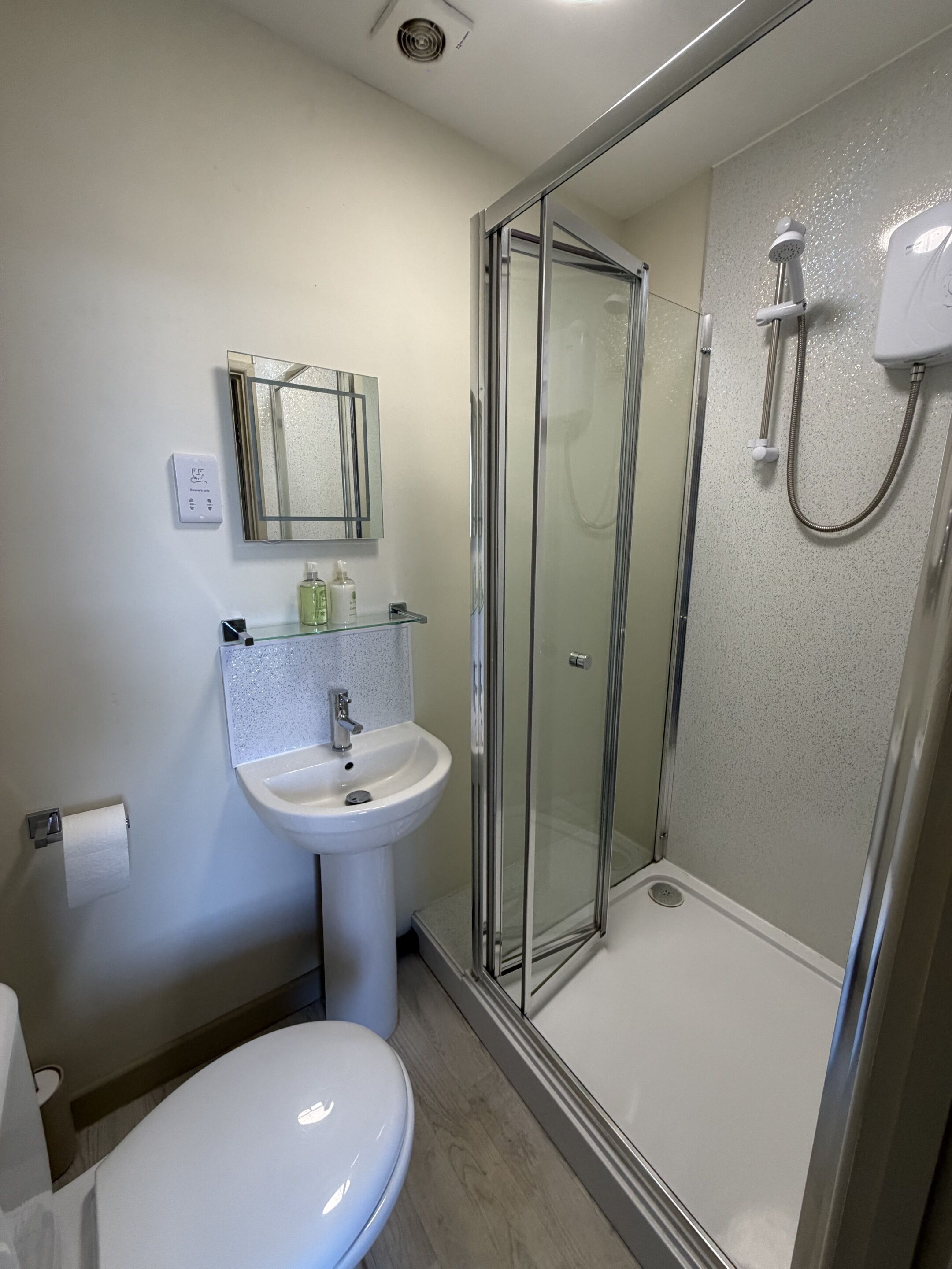 Ein Badezimmer mit Duschkabine, Waschbecken, Toilette und Spiegel.