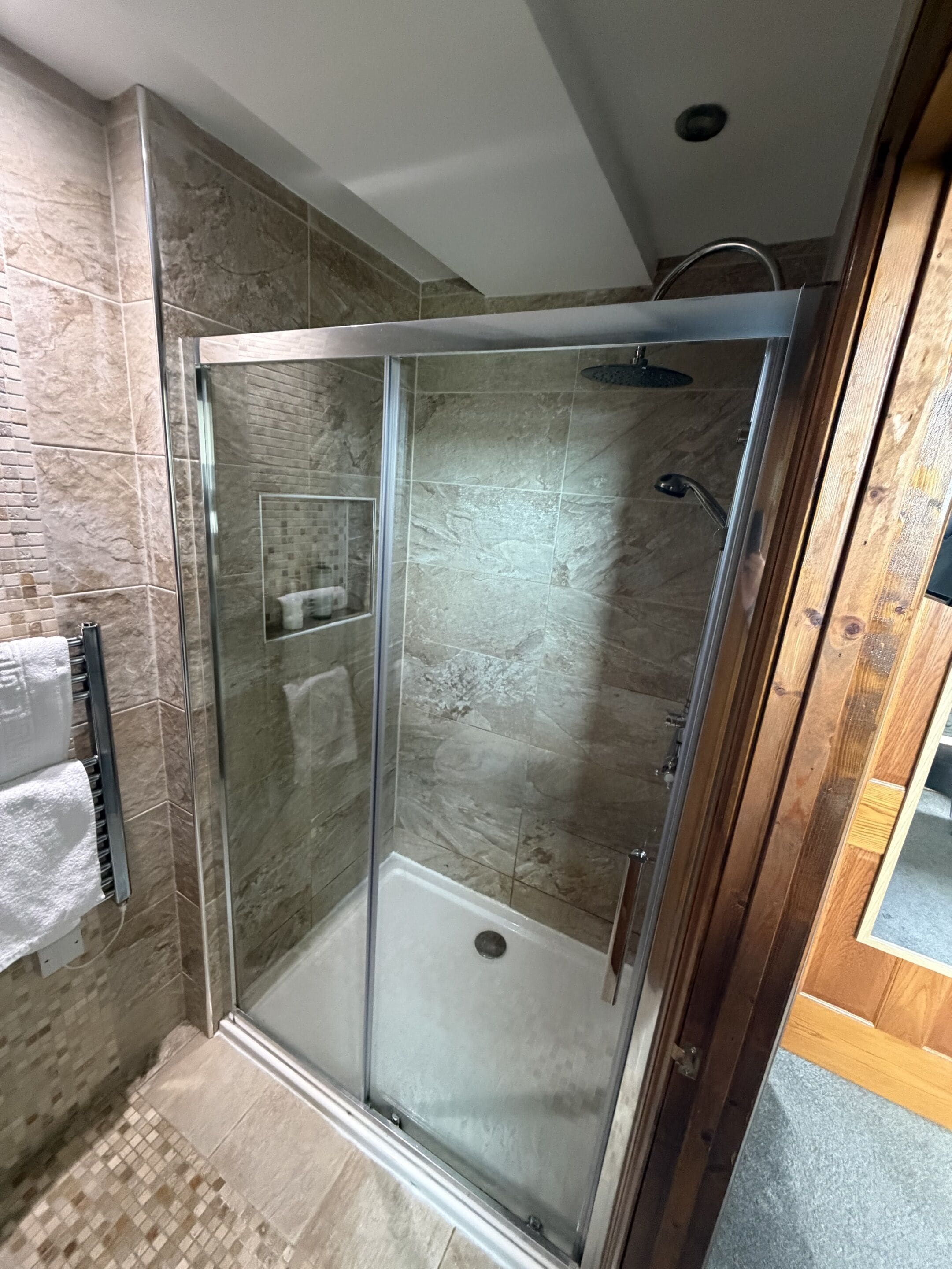 A glass-enclosed shower stall with a showerhead, a towel rack with towels, and a shower control panel.