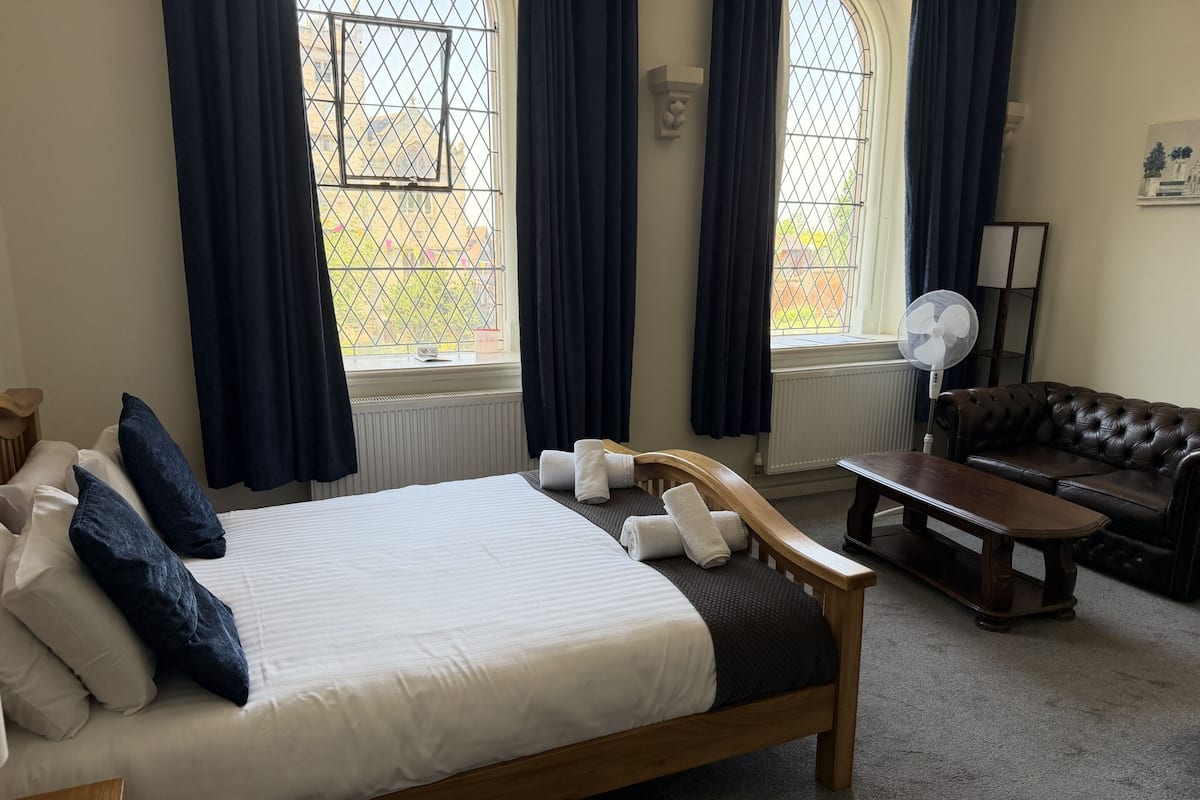 Une chambre à coucher avec un lit en bois, un canapé en cuir, une table basse en bois et un ventilateur sur pied.