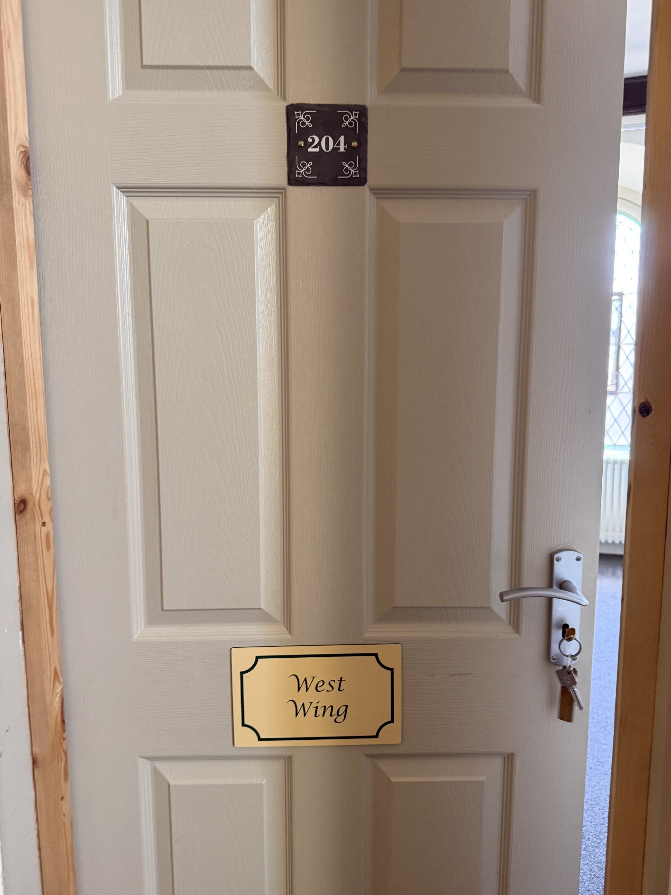 A door with a number plate labeled '204' and a sign below it reading 'West Wing.'