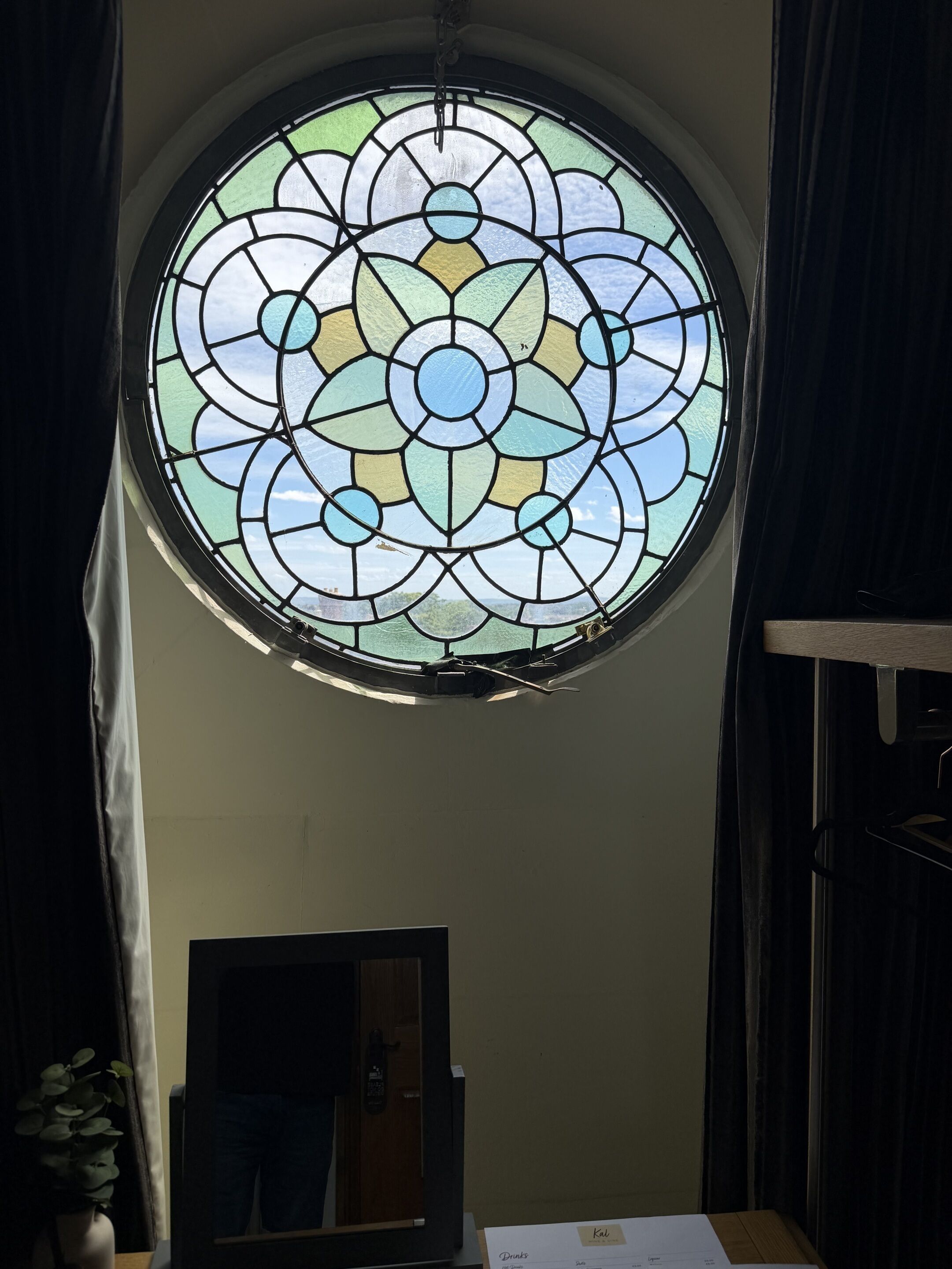 A circular stained glass window with a geometric pattern, a wooden door below, and a potted plant to the left.