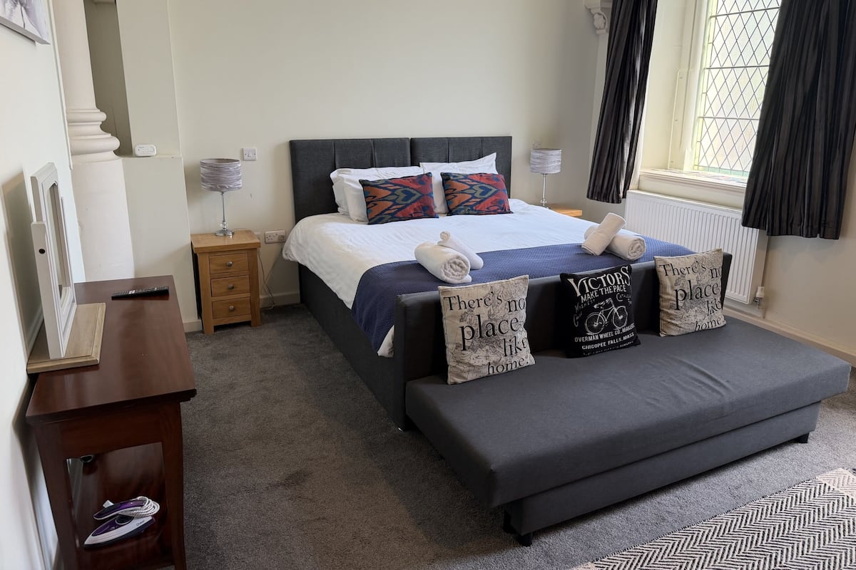 Une chambre à coucher bien aménagée, avec un lit, des tables de chevet, un banc et des coussins décoratifs.