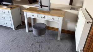 Een kamer met een wit bureau, een grijze poef, een radiator en een televisie.