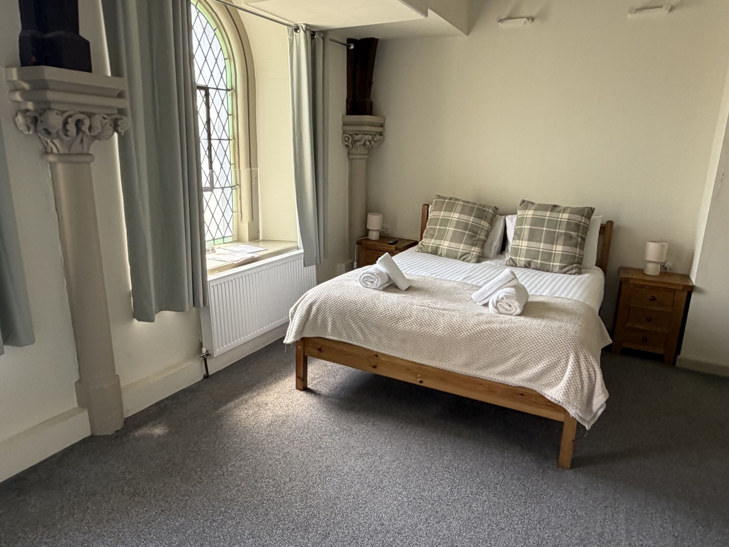 A bedroom with a wooden bed, two nightstands, a window with curtains, and a radiator.