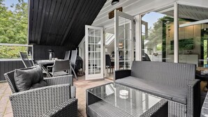 An outdoor patio area with wicker furniture, a glass table, and a view of the interior kitchen through glass doors. - Awesome home in Skjern with WiFi (Skjern)