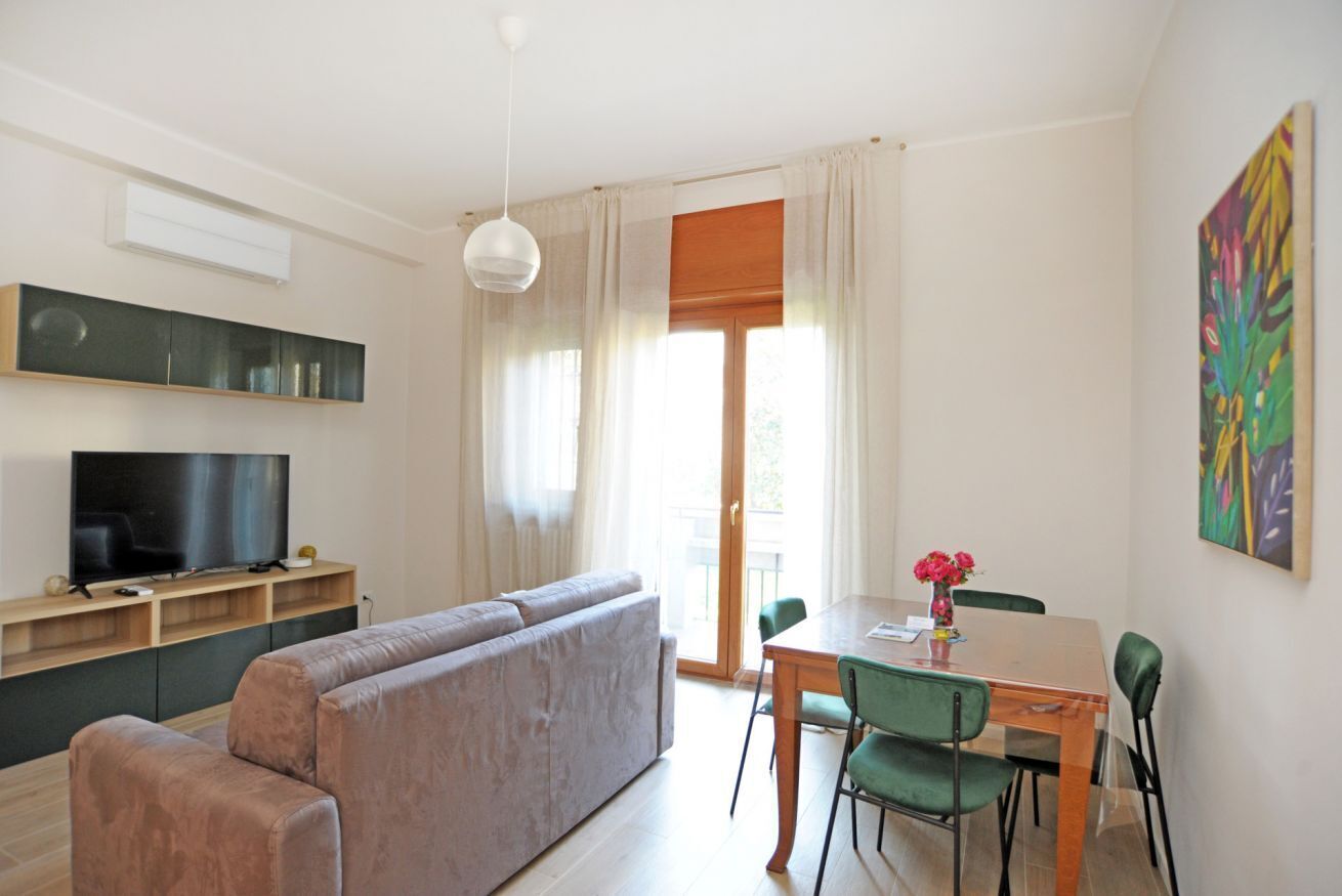 A living room with a sofa, TV, dining table, chairs, and a painting on the wall.