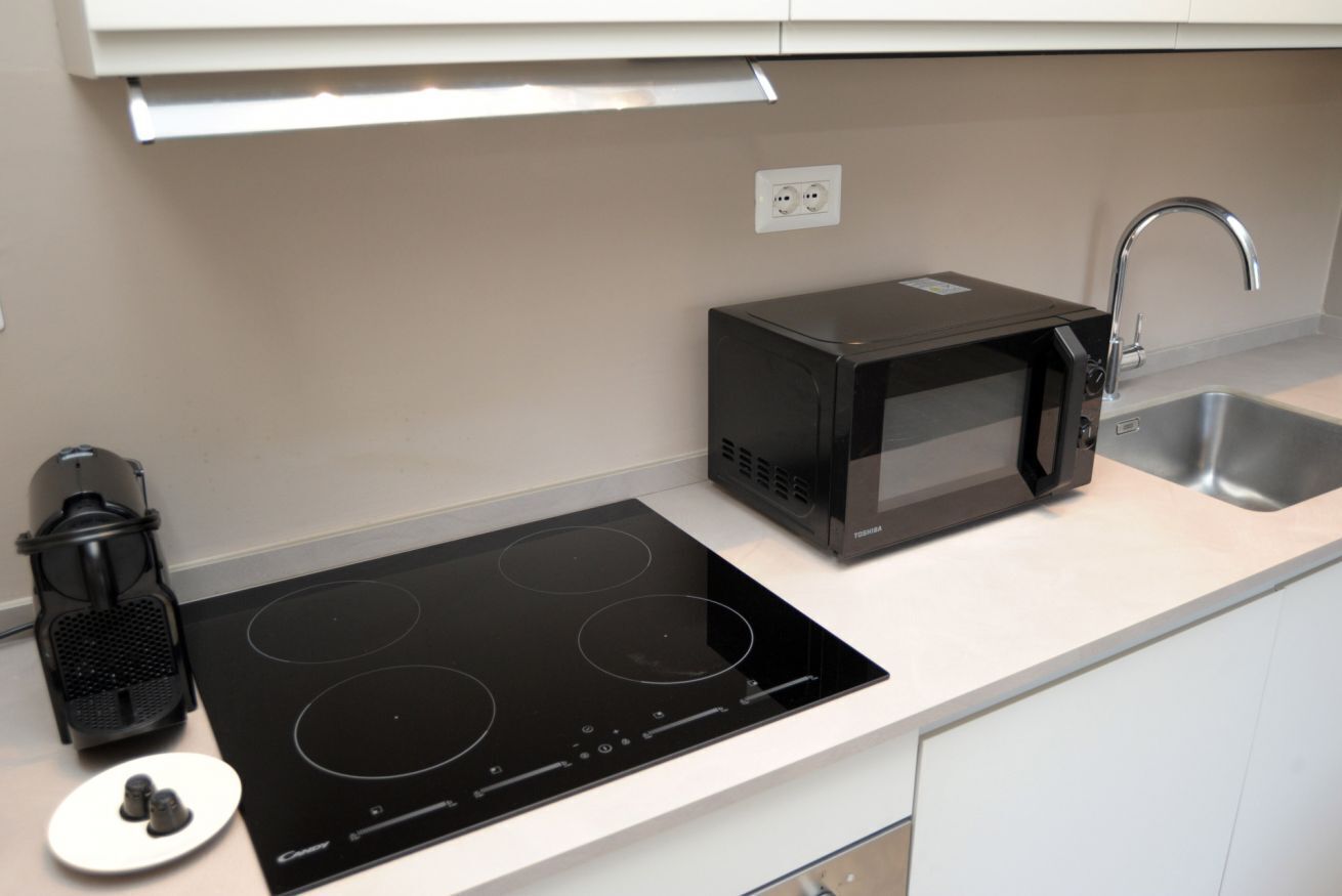 Cozinha com fogão por indução preto, micro-ondas, máquina de café e pia.