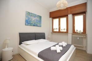 A bedroom with a bed, a nightstand, a lamp, a painting, and a window with curtains.