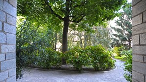 A paved pathway leading to a building entrance, surrounded by lush greenery and trees. - Gambara Apartment Travel Inside (Milano)