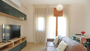 A modern living room with a flat-screen TV, wooden entertainment unit, a leather sofa, and a dining area with a table and chairs. - Gambara Apartment Travel Inside (Milano)