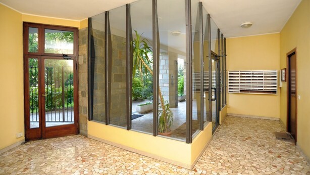 A room with a tiled floor, a glass partition, a door with a metal gate, and a window with blinds. - Gambara Apartment Travel Inside (Milano)