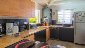 A modern kitchen with wooden cabinets, a built-in oven, a dishwasher, and a refrigerator. - Tropical escape in an authentic Creole villa with private saltwater pool. (Anse-Bertrand)