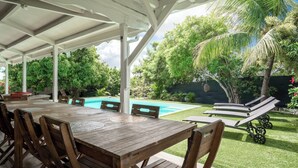 A covered outdoor area with a pool, wooden tables and chairs, and lounge chairs. - Tropical escape in an authentic Creole villa with private saltwater pool. (Anse-Bertrand)
