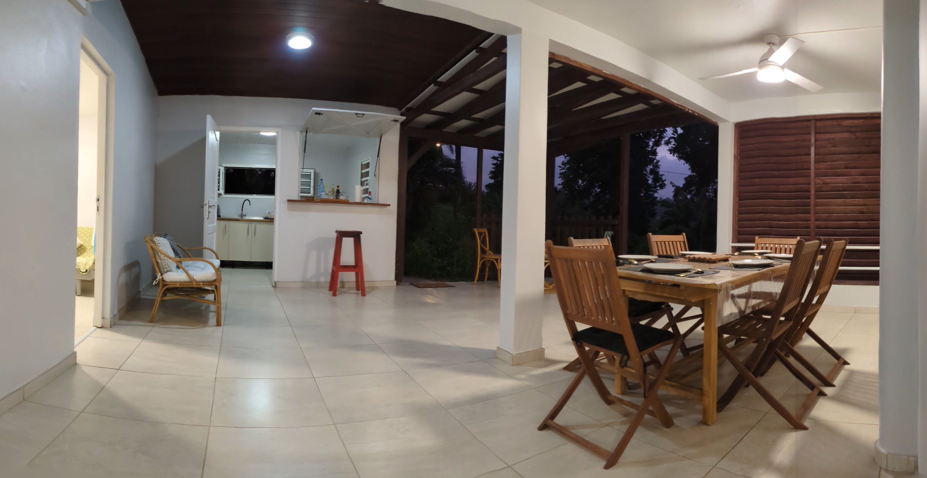 Un'ampia sala da pranzo con un tavolo e sedie in legno, una cucina sullo sfondo e vista all'esterno.