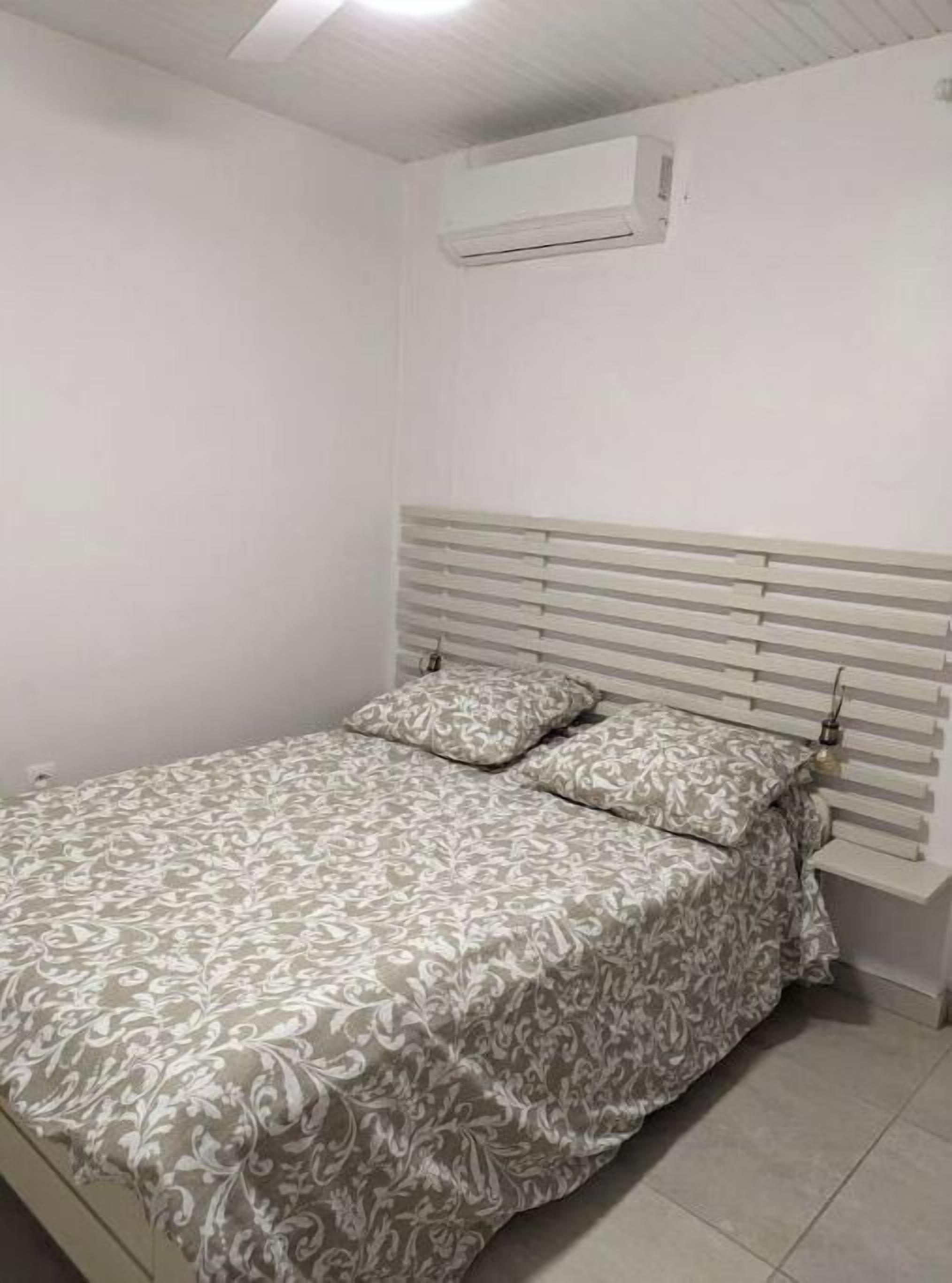A bedroom with a bed, a headboard, and an air conditioning unit on the wall.