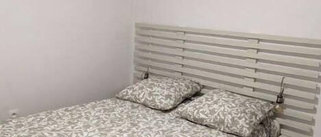 A bedroom with a bed, a headboard, and an air conditioning unit on the wall.