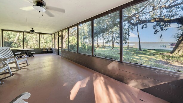 A covered outdoor area with a ceiling fan, large windows, and a view of a lake and trees. - Lakefront home on Lake Kerr near Salt Springs with large porch and great yard (Salt Springs)