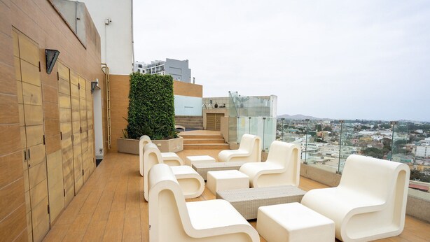 A rooftop terrace with modern white furniture, a glass balustrade, and a view of the city. - Redibuk - Nice 1BR apartment in Barranco (Lima)