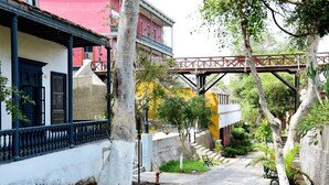 A narrow street with buildings on either side, a bridge overhead, and trees lining the path. - Redibuk - Nice 1BR apartment in Barranco (Lima)