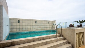 A rooftop swimming pool with steps leading down to the water, a tiled wall, and a planter with plants. - Redibuk - Nice 1BR apartment in Barranco (Lima)