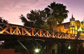 A bridge with a metal truss structure, leading to a building with a domed roof and a cross at the top.