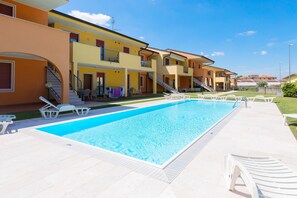 Una piscina con lettini, una scala e un edificio con balconi.