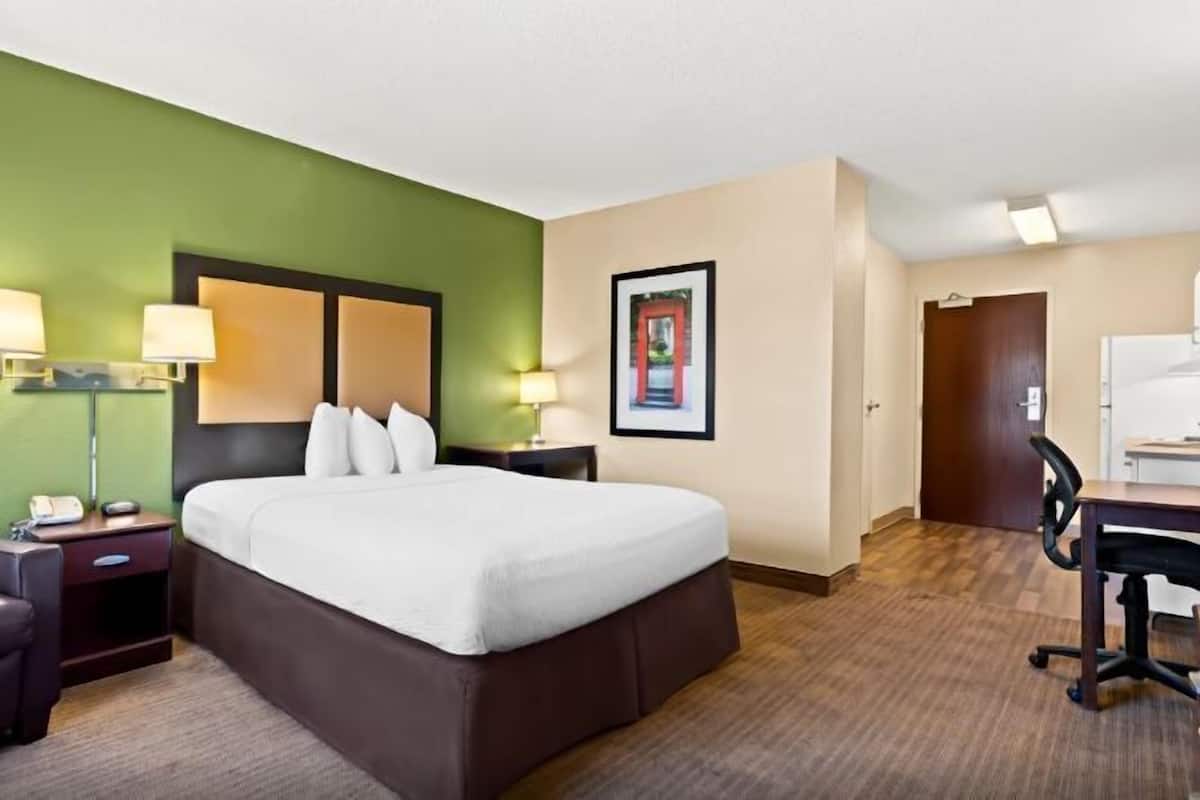 Une chambre d’hôtel avec un lit, un bureau, une chaise, une lampe et un tableau au mur.