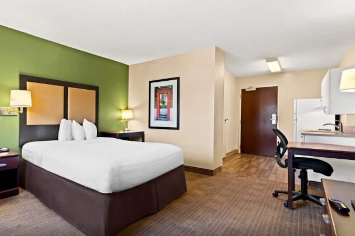 Habitación de hotel con cama, escritorio, silla, lámpara y un cuadro en la pared.