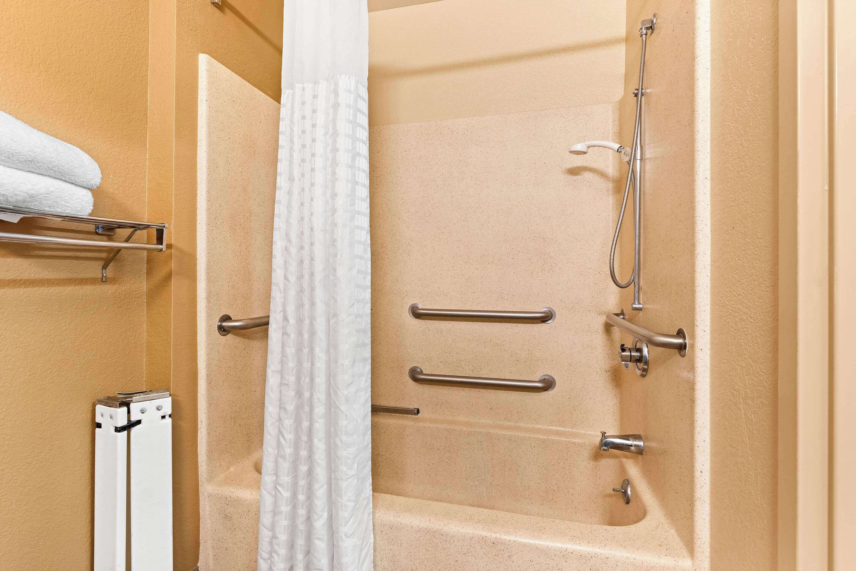 A bathroom with a bathtub, shower, and handrails.