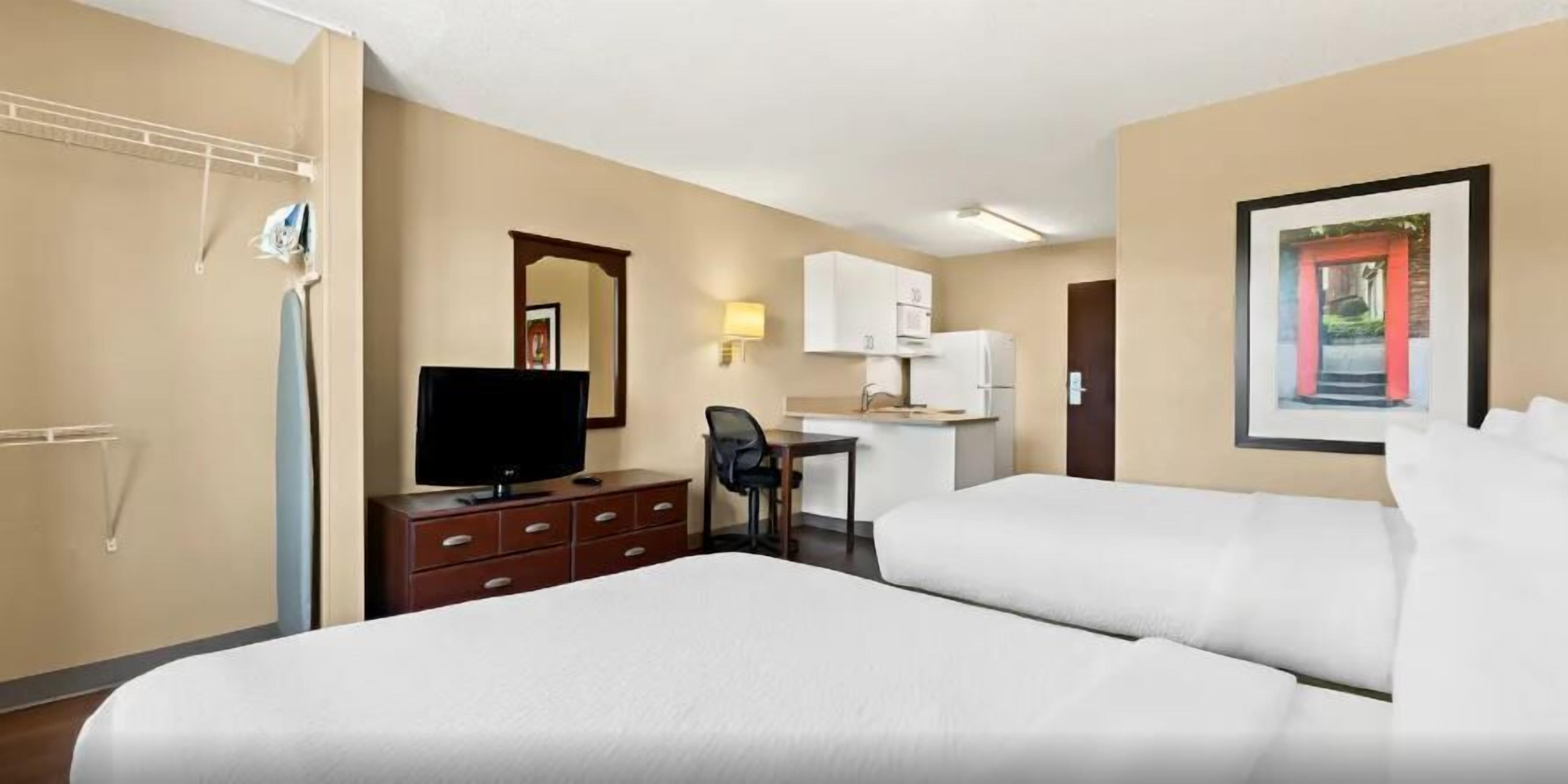 Een hotelkamer met twee bedden, een bureau, een televisie, een kledingkast en een lijst aan de muur.
