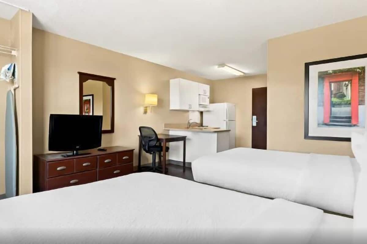 Une chambre d’hôtel avec deux lits, un bureau, une télévision, une armoire et un tableau encadré au mur.