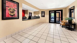 A hotel lobby with a reception desk, a seating area with a chair and a table, and a large framed artwork on the wall. - Suburban Studios Columbus Fort Benning Area (Columbus)