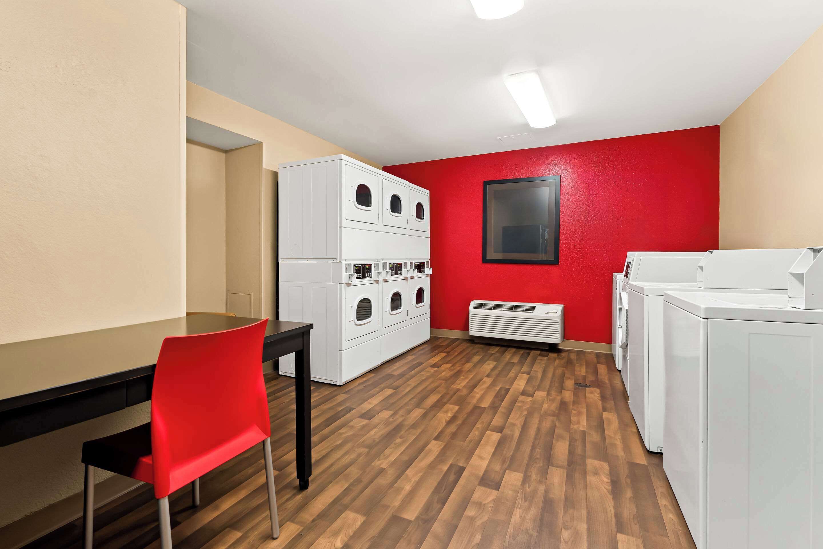 Ein Waschraum mit roter Wand, einer weißen Waschmaschine und einem Trockner, einem weißen Schrank mit mehreren Fächern und Holzboden.
