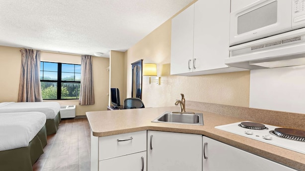A hotel room with a kitchenette, a bed, a desk, and a window with curtains. - Suburban Studios Columbus Fort Benning Area (Columbus)