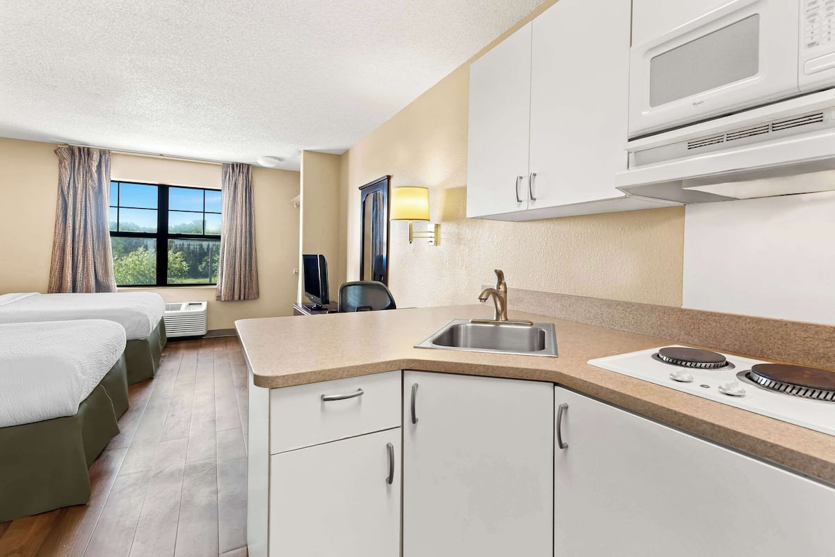 Une chambre d’hôtel équipée d’une kitchenette, d’un lit, d’un bureau et d’une fenêtre avec des rideaux.