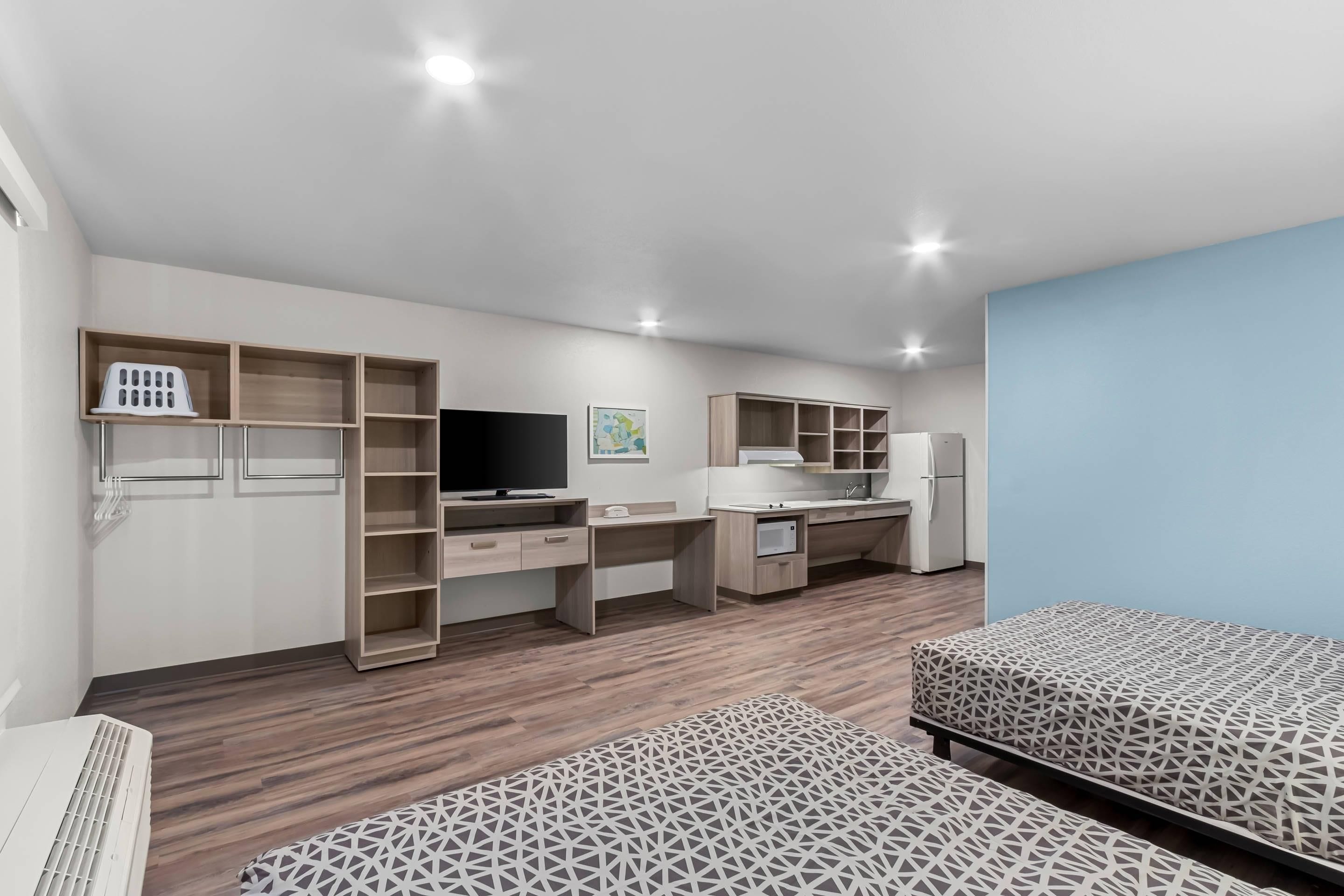 Una habitación moderna y luminosa, con escritorio, computadora, televisión y kitchenette.