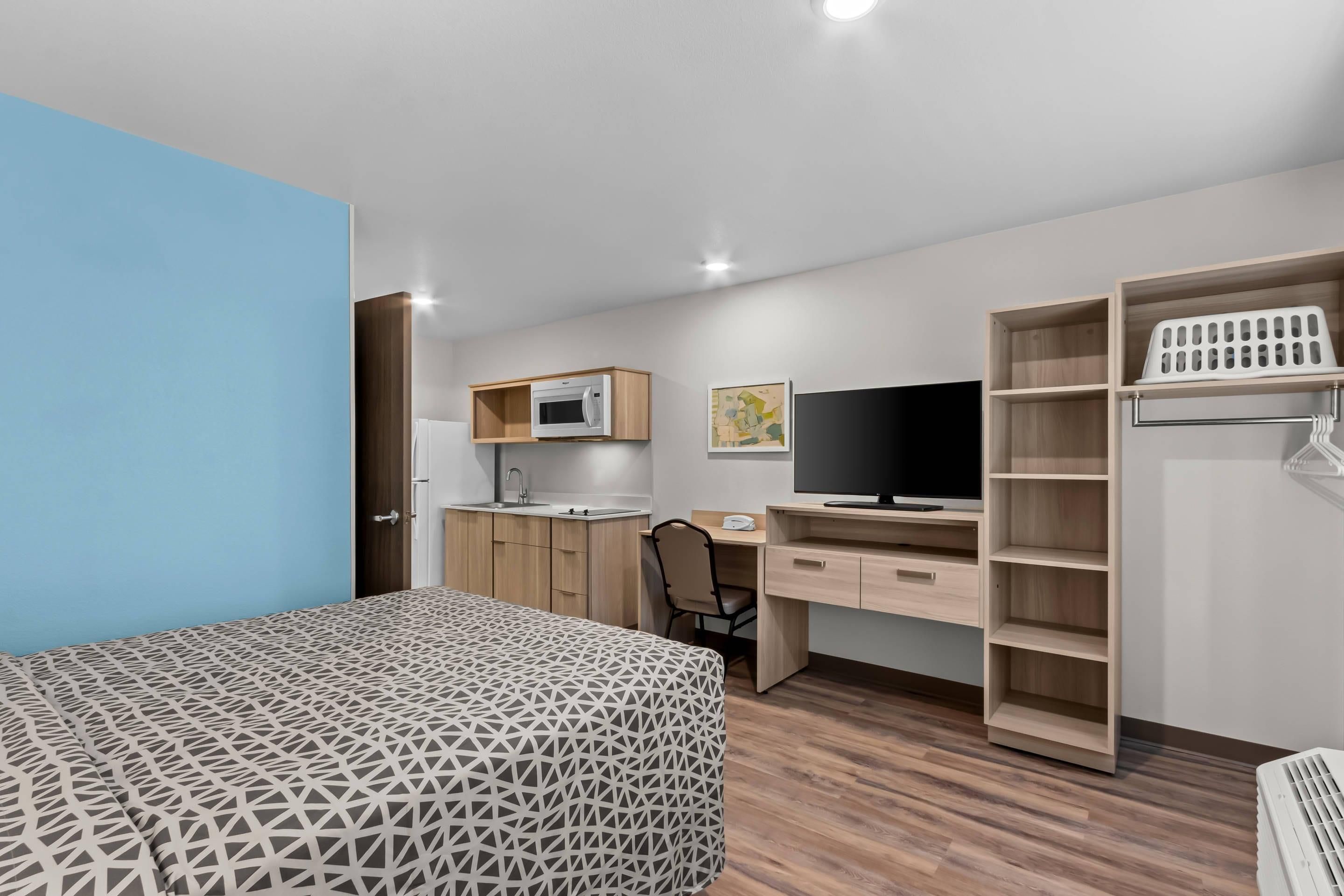 Habitación pequeña y funcional con cama, escritorio, televisor, microondas y armario.