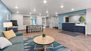 A modern living room with a sofa, a round coffee table, and a dining area with chairs and a table. - Woodspring Suites Gilbert - Mesa Gateway Airport (Gilbert)