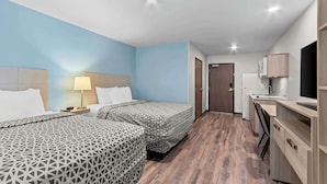 A hotel room with two beds, a desk, a chair, a TV, and a kitchenette. - Woodspring Suites Gilbert - Mesa Gateway Airport (Gilbert)